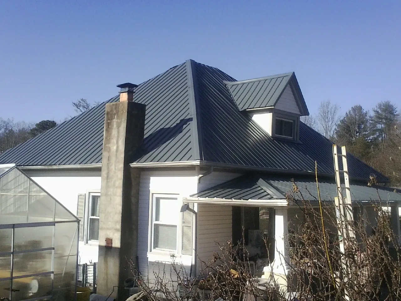 Dark blue standing seam metal roof on a white farmhouse with dormer — Slate & Tile Roof Repair by Roofing Brothers in College Point