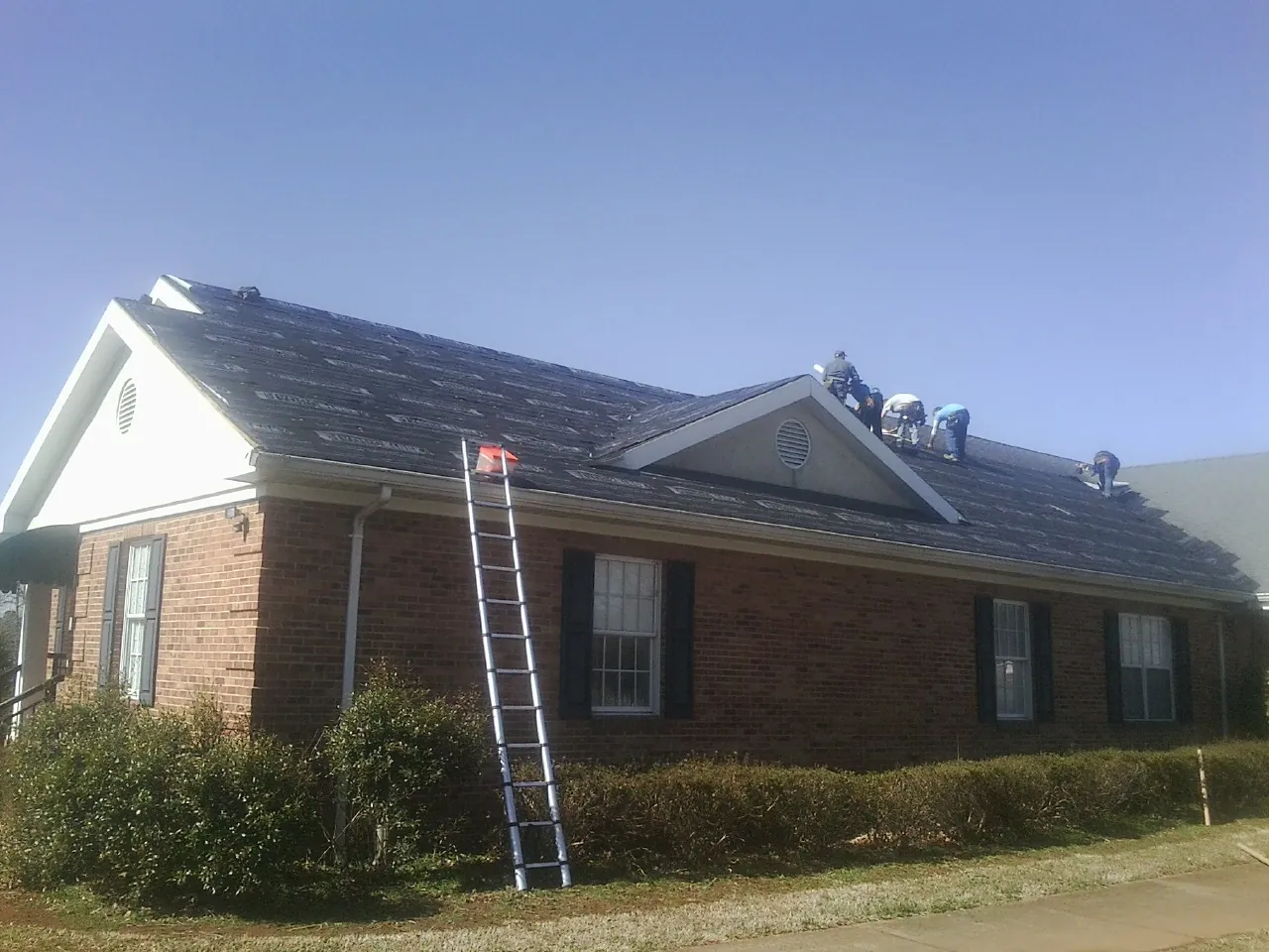 Crew tearing shingles off a brick ranch roof with a ladder set — Metal Roof Repair work by our crew in College Point