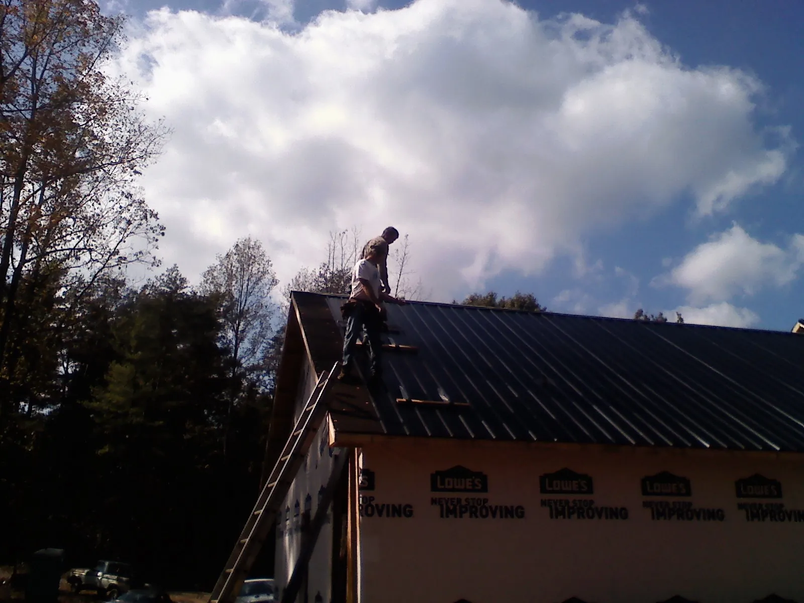 Roofer fastening dark metal panels high against a cloudy sky, from a Roof Inspection job in College Point