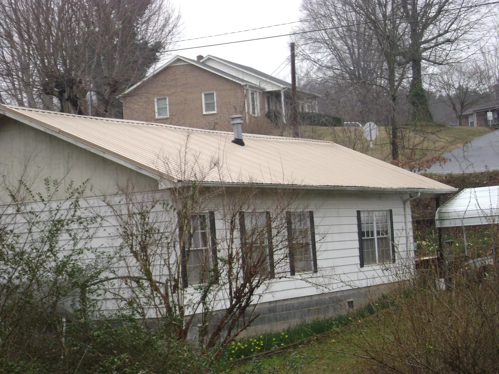 Tan metal roof on a white sided house set into a hillside — Commercial Roofing by Roofing Brothers in College Point